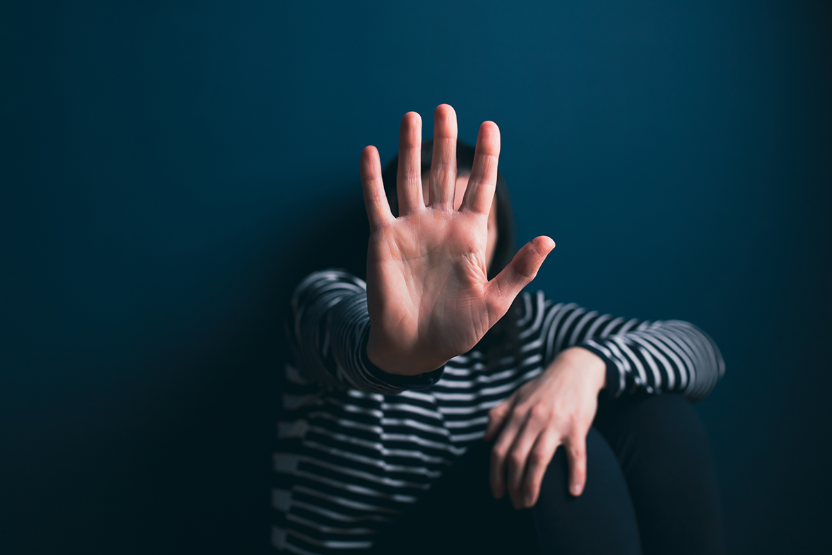 Kvinna sitter i ett mörkt rum och sträcker ut sin hand som ett stopptecken. 